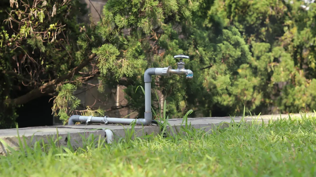 Outdoor well water spigot and supply pipes beside a grassy yard
