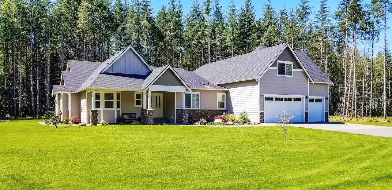 Ranch-style home with a two-car garage and wide lawn in front of tall evergreen trees