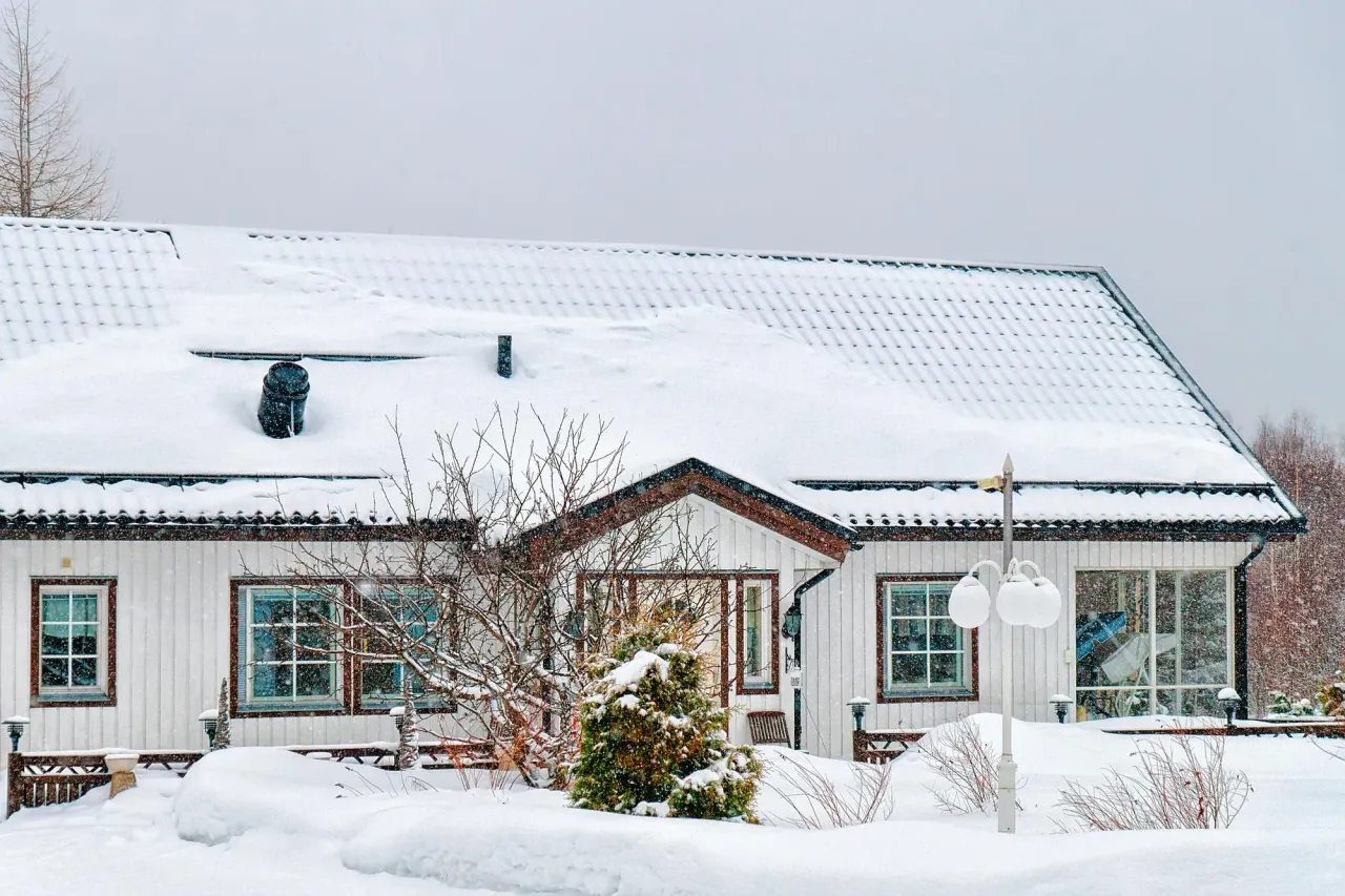 Single-story white house with a snow-covered roof during a winter snowfall