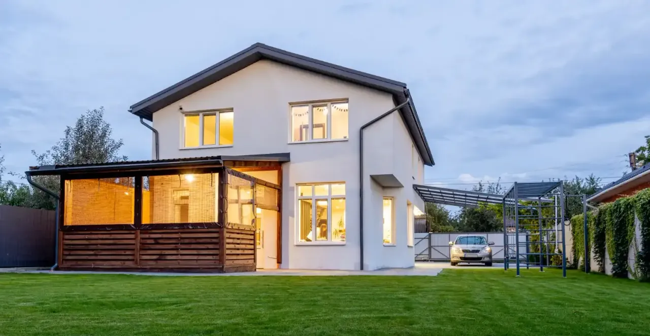 Two-story white house with a lit covered patio and a wide lawn at dusk