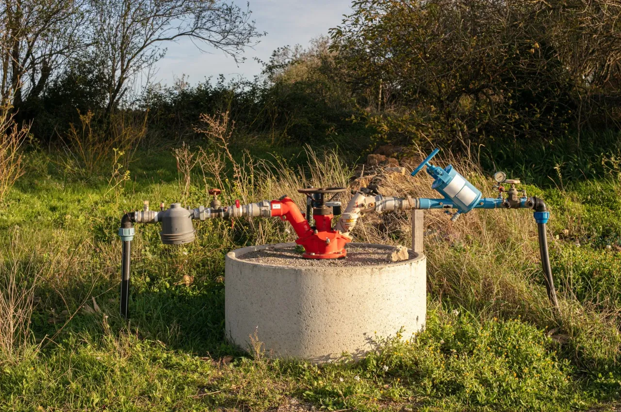 Well head on a concrete base with water pump piping and valves in a grassy field