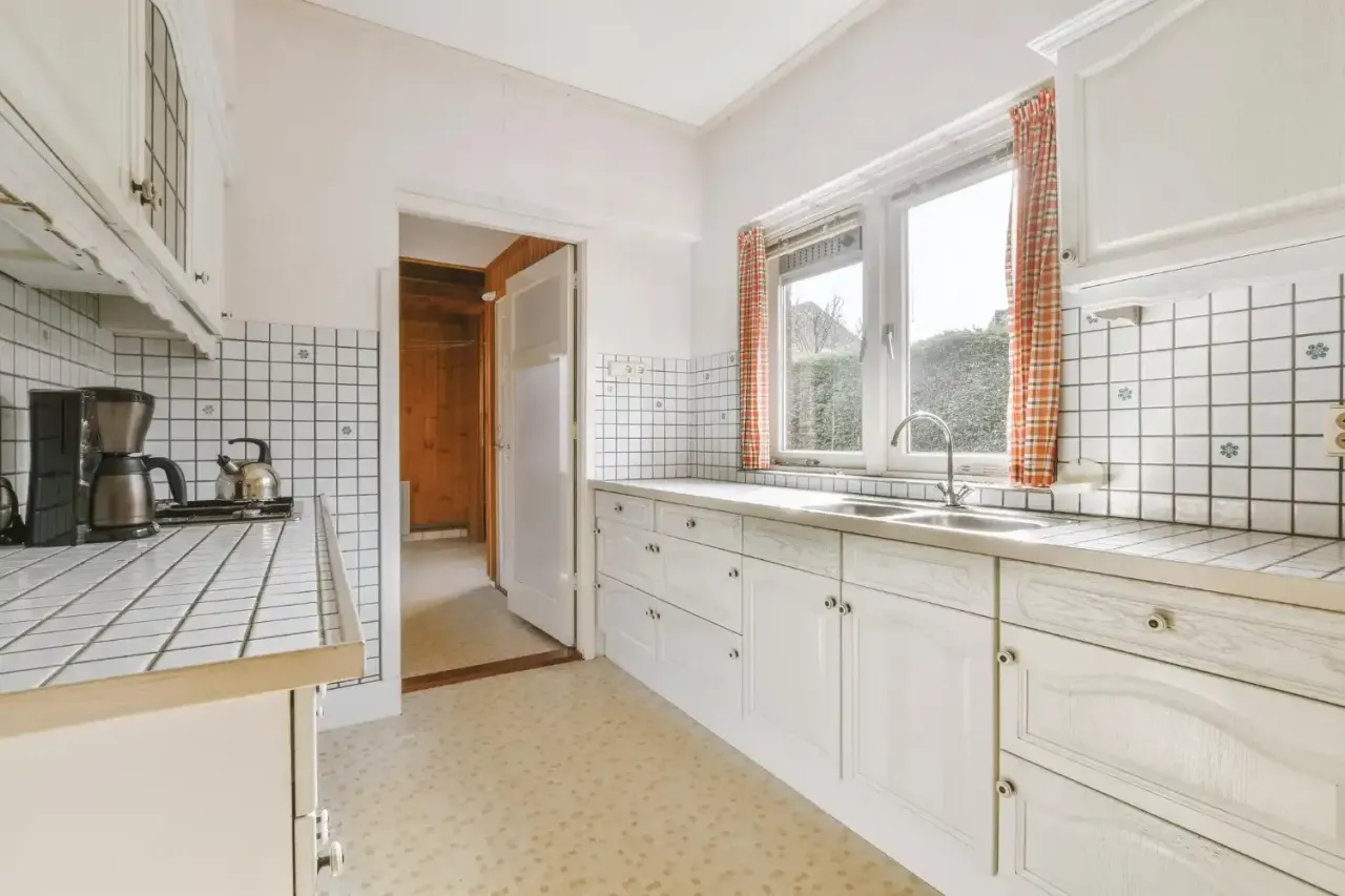 White galley kitchen with tiled counters and a window over the double sink